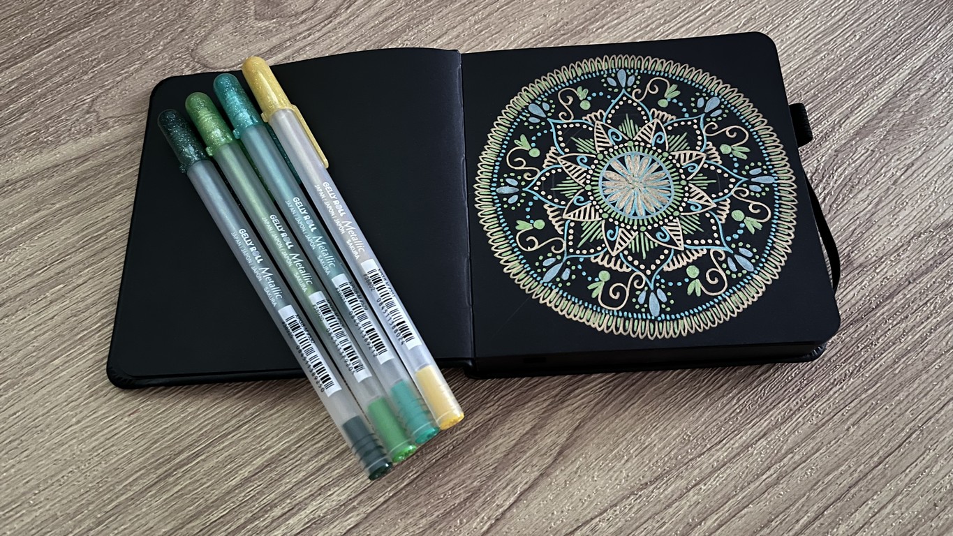 Photo of four Gelly Roll Metallic Pens With a Small Black Paper Sketchbook
